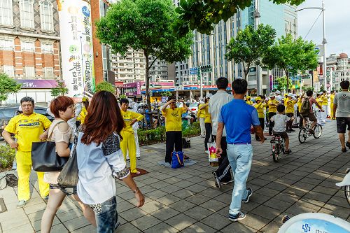 环绕明诚公园四周展开“功法长城”，演示法轮功五套舒缓优美的动作；群众放慢脚步观赏。