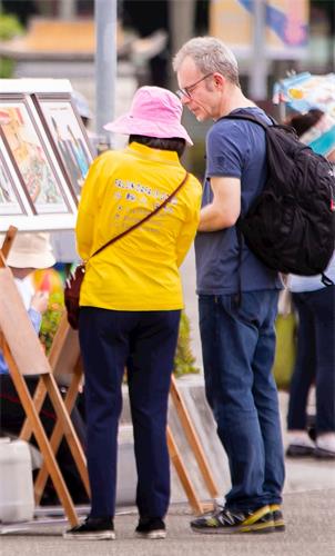 '图11：从瑞士来台旅游的 丹尼先生（Danny，右）观看图片展，透过学员的解说，明白了些大法洪传的情况。'